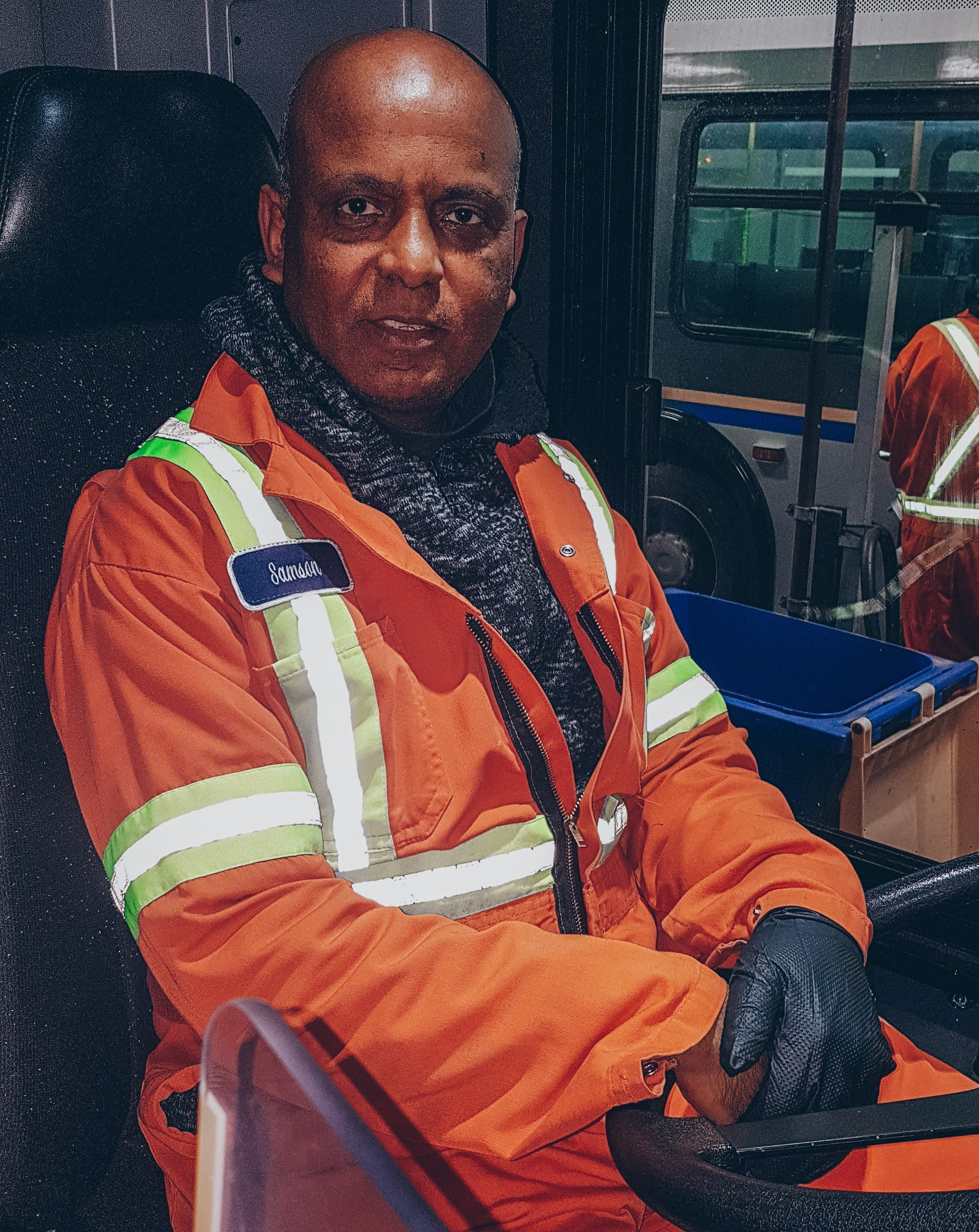 Sammy posing for a photo while sitting in the driver's seat of a bus