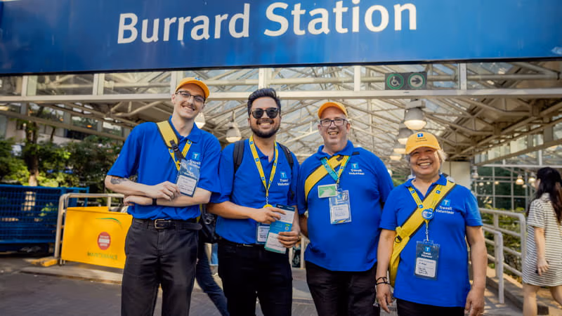 Four TransLink volunteers are smiling at the camera in front of Burrard Station.