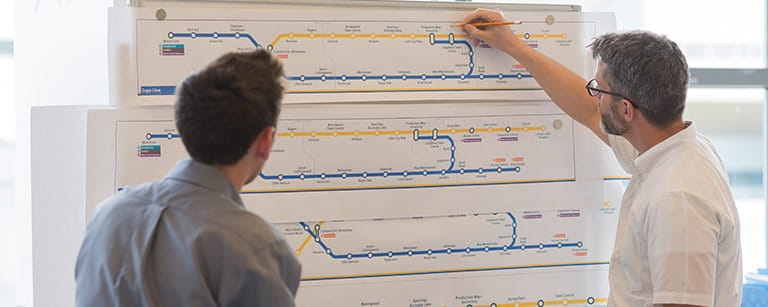 Two male co-workers planning train routes on a transit map