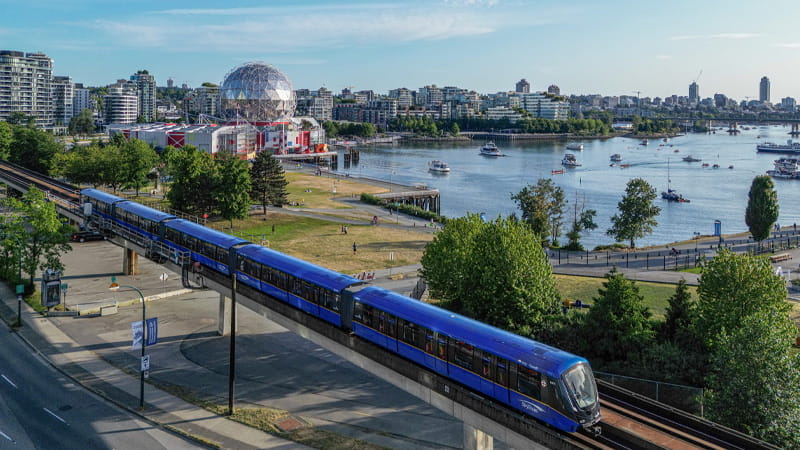New Mark V train travels along the waterfront with a city skyline in the background