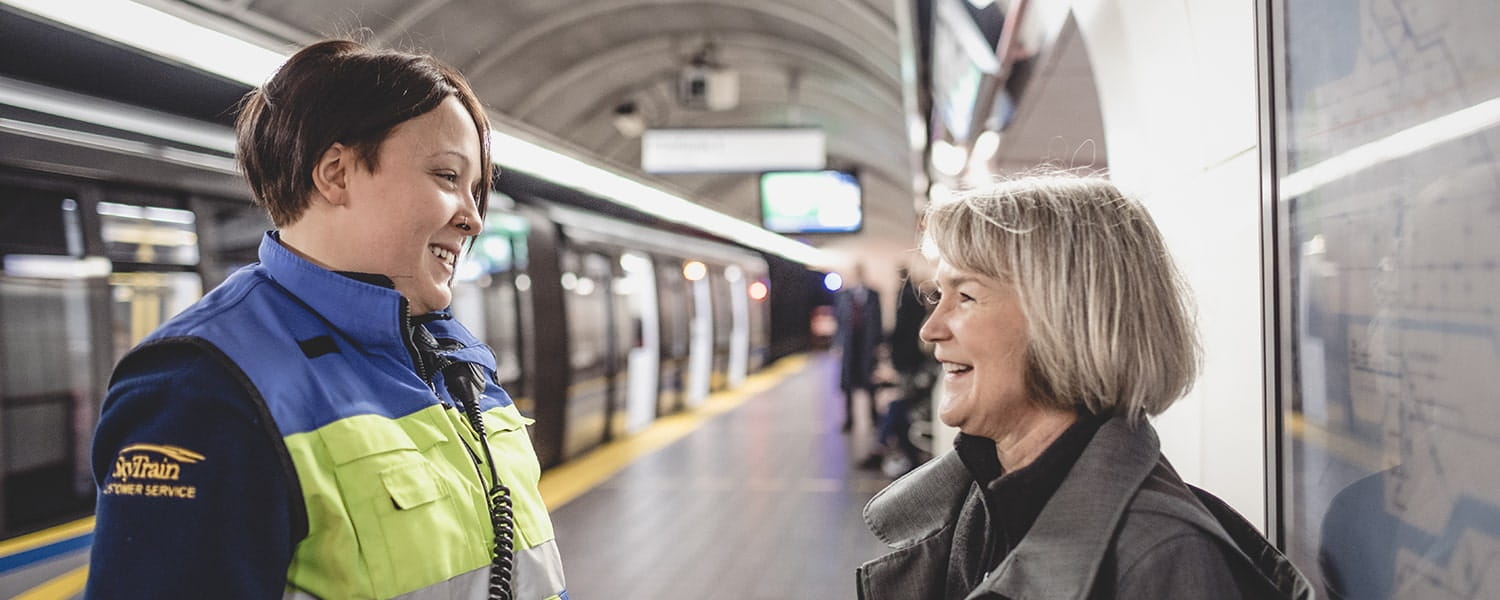 A SkyTrain Attendant speaking to a customer at a train station