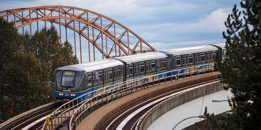 A new SkyTrain running on an elevated rail with an orange bridge in the background