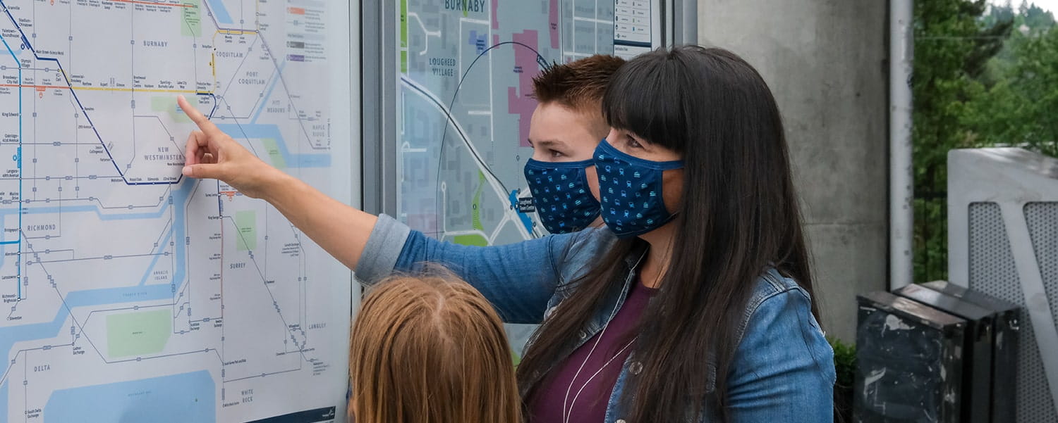 A family of three all wearing TransLink branded face masks and looking at direction on a map