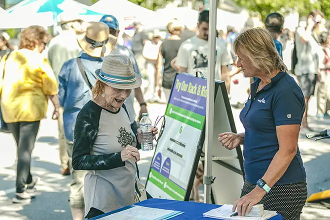 A TransLink employee assisting an older lady at an outdoor booth