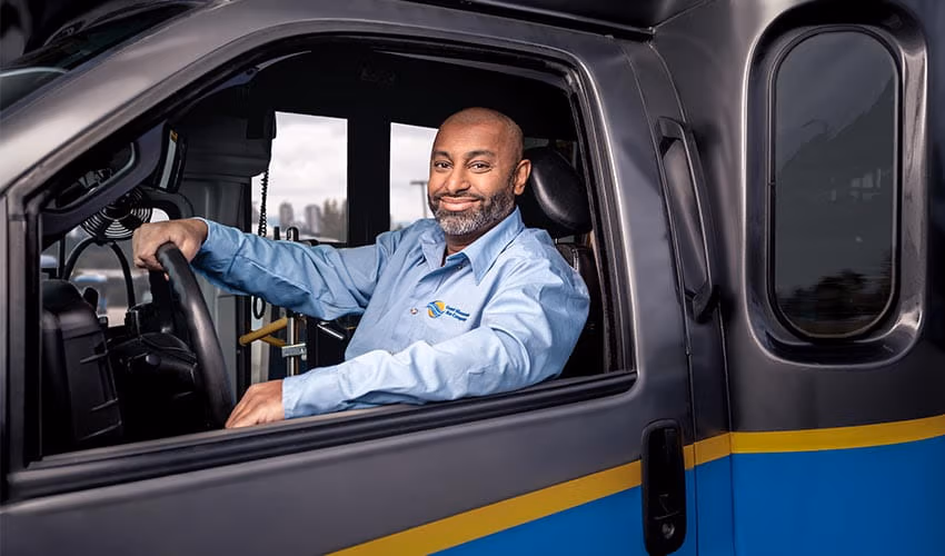 A smiling CMBC Community Shuttle Driver sitting confidently behind the wheel of a shuttle bus