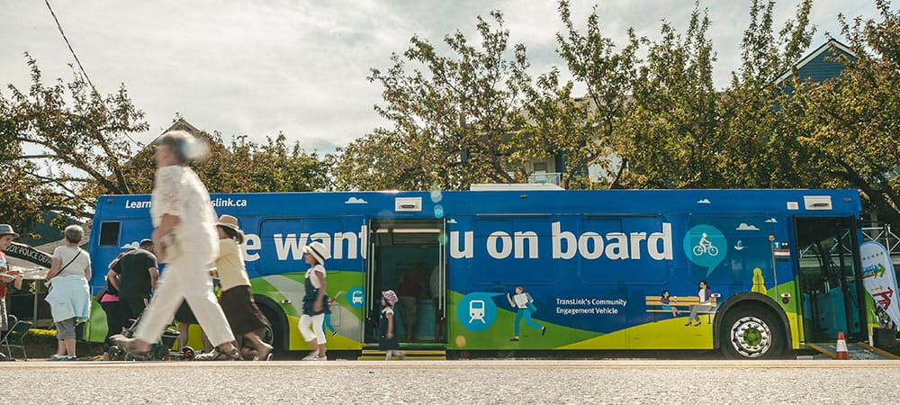 A multi coloured public engagement bus parked in the public with people walking by