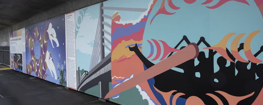 Indigenous art murals on the side of a wall, one illustrating a group of people canoeing