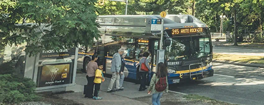 Passengers boarding a bus parked beneath the Expo Line near King George station on a sunny summer day