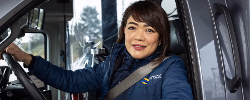 Bus operator in a blue jacket sits in the driver’s seat, smiling at the camera.