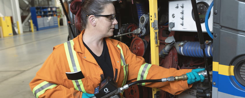 A heavy duty mechanic, dressed in a work gear suit, is inspecting and performing maintenance on a bus.