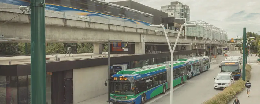 A SkyTrain approaching a station while a bus waits below