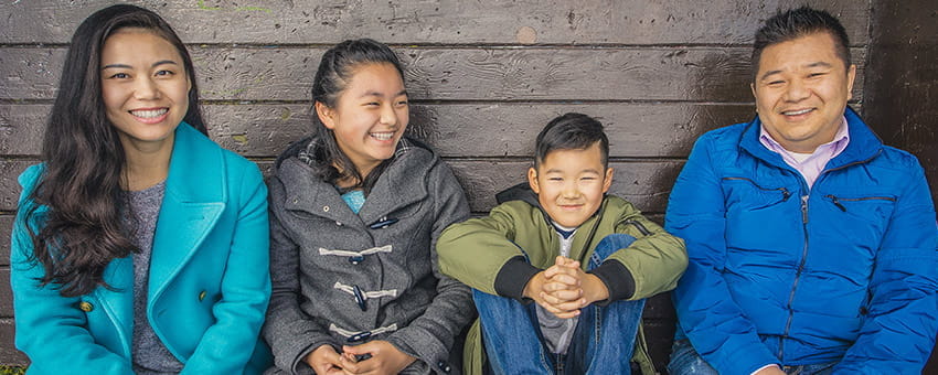 Smiling family of four, sitting together at a transit stop exploring Metro Vancouver's transit system.