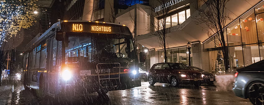 TransLink NightBus driving on a rainy city street at night.