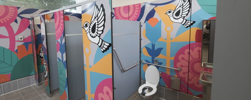 Accessible public restroom stalls with brightly colored murals featuring geometric floral patterns and a bird illustration on the doors.