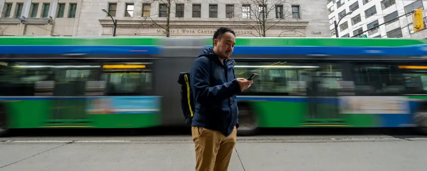 A man engaged on his phone as a RapidBus speeds behind him, creating a motion blur
