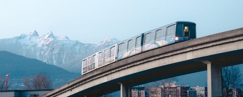 SkyTrain is on the overhead guideway. Snow capped mountains in the background.