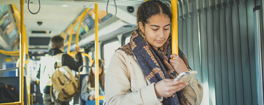 A young woman on the bus wearing a mask and looking at her mobile phone