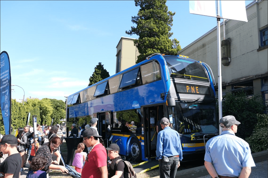 Double-decker bus parked at PNE fairgrounds with crowd of people near it.