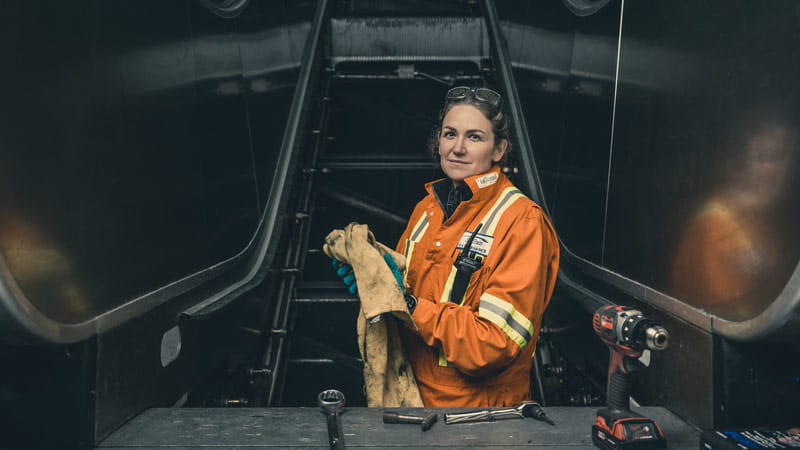 A mechanic works at the base of an escalator in orange coveralls