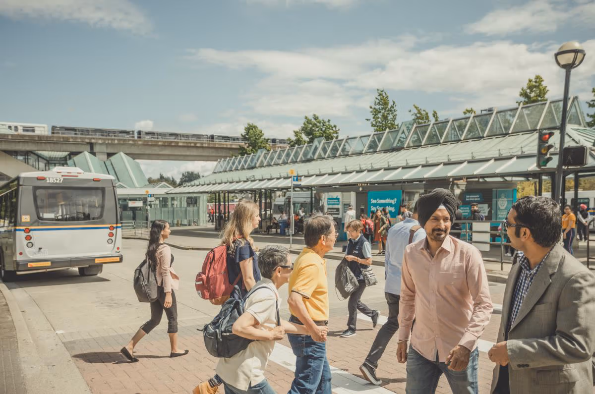 Passengers milling about at the Surrey Central bus loop on a sunny day