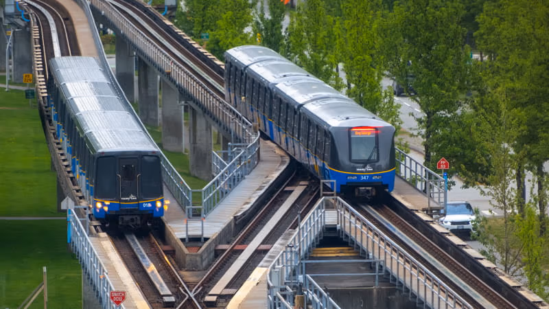 Two SkyTrains on tracks surrounded by greenery.