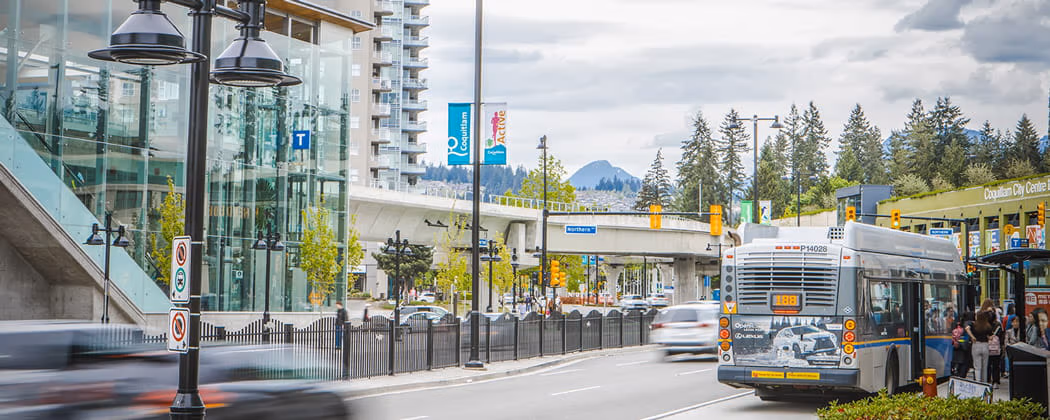 A bus parked at a bus bay in front of a SkyTrain station on a bright and sunny day