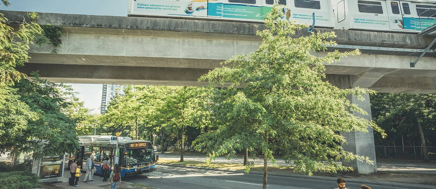 People boarding a bus underneath the SkyTrain rail on a summer day
