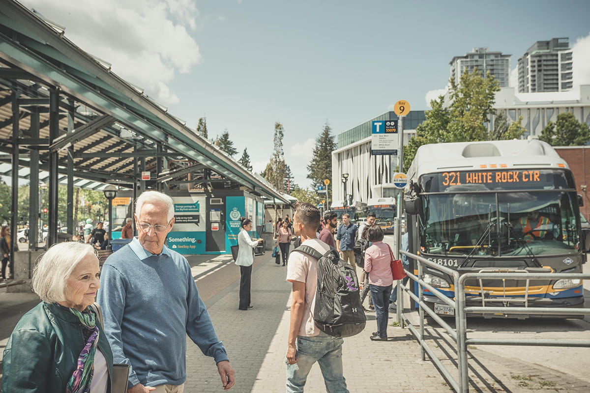 People walking around a bus exchange with the 321 parked next to a bus stop in the distance