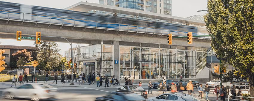 A bustling intersection with pedestrians, cars, and the SkyTrain gliding along the guideway