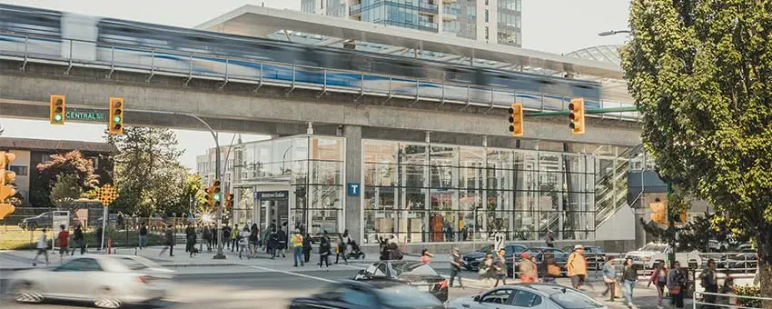 A bustling intersection with pedestrians, cars, and the SkyTrain gliding along the guideway