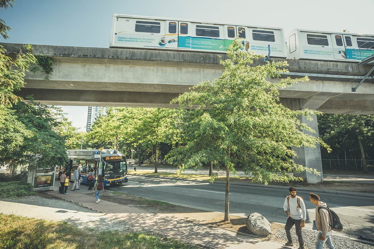 Passengers boarding a bus parked beneath the Expo Line near King George station on a sunny summer day