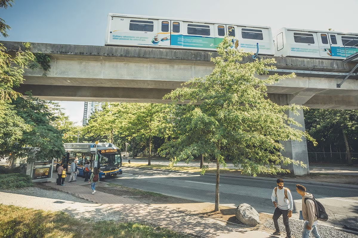 Passengers boarding a bus parked beneath the Expo Line near King George station on a sunny summer day