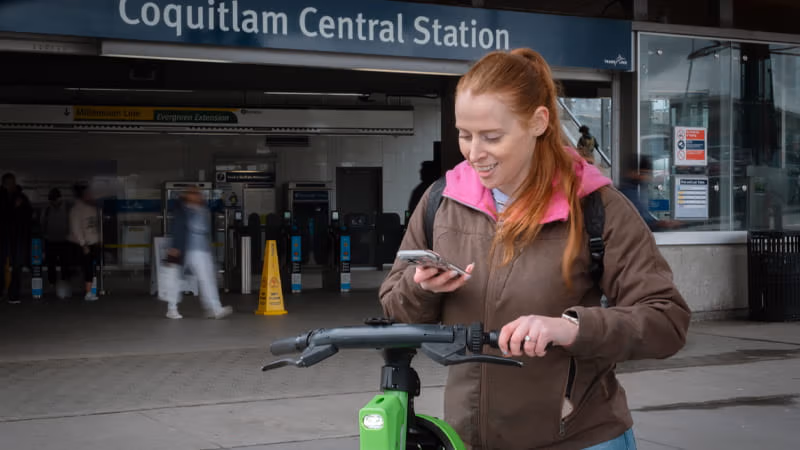 Customer looking at her phone with an e-bike in front of Coquitlam Central Station