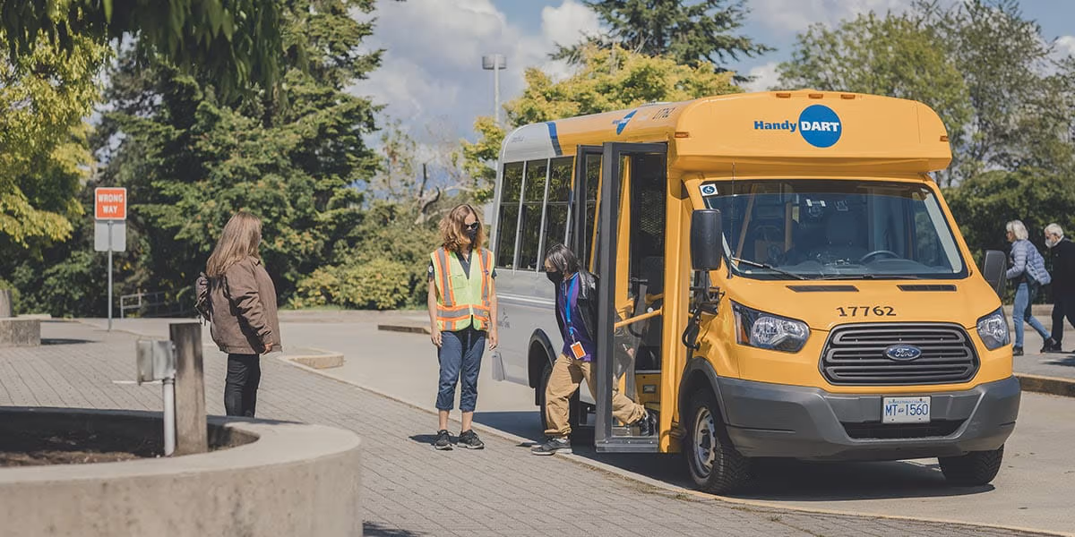 A man exiting a HandyDART vehicle while the driver is standing by for support.