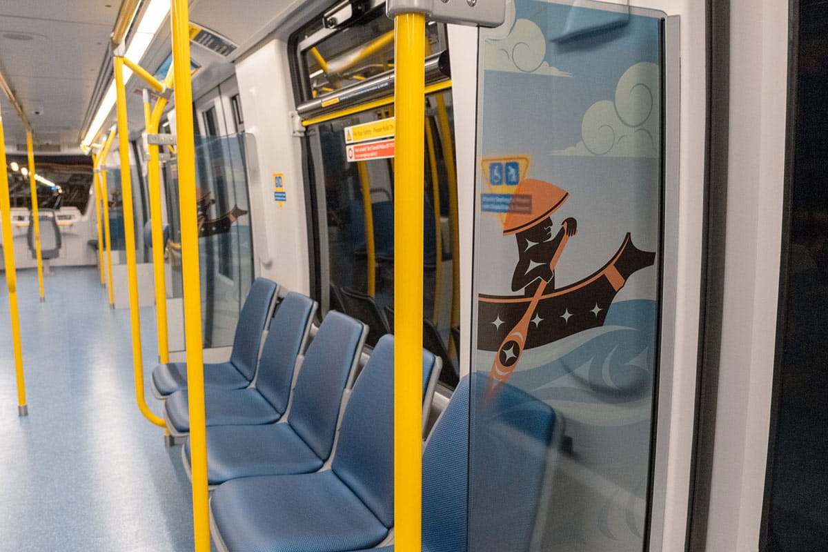 Indigenous artwork of a canoe journey with figures paddling across a sea filled with marine life on a Mark V SkyTrain Car