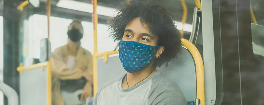 A young man wearing a mask looking out the window of the bus