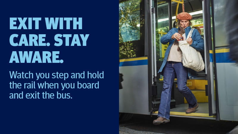 Woman steps off a bus while holding the handrail. Text on the image reads: “EXIT WITH CARE. STAY AWARE. Watch your step and hold the rail when you board and exit the bus.”