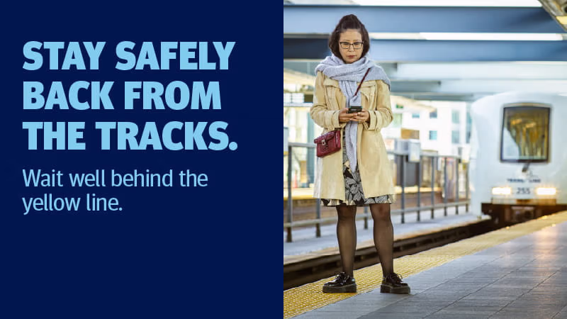 A woman stands on a train platform behind the yellow safety line as a train approaches.