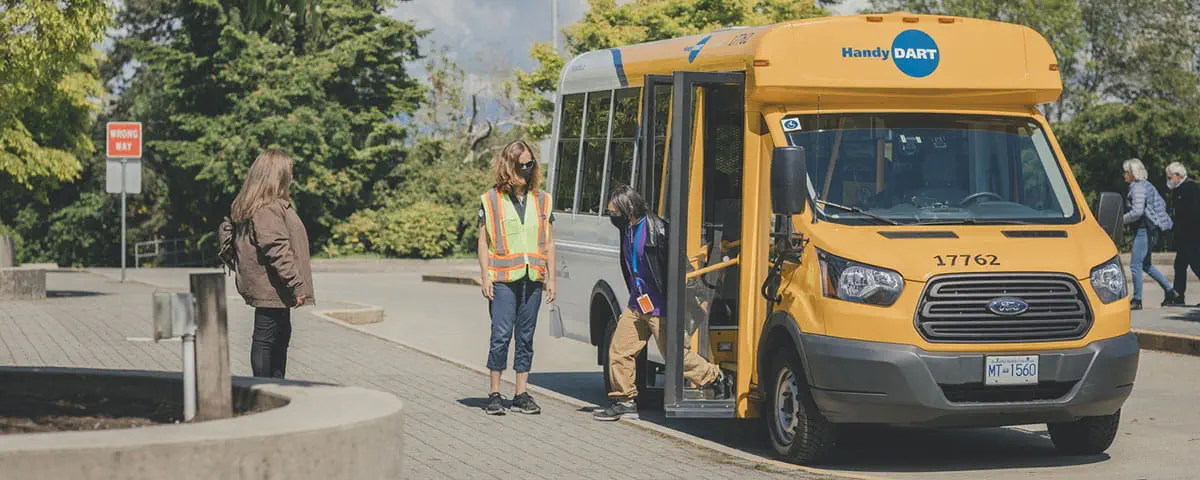 A man exiting a HandyDART vehicle while the driver is standing by for support.