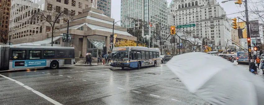 Two buses downtown during rainy weather with a grey umbrella in the foreground