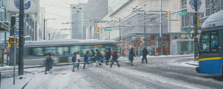 Pedestrians crossing Robson Street at Granville Street during snowy weather with two buses in frame