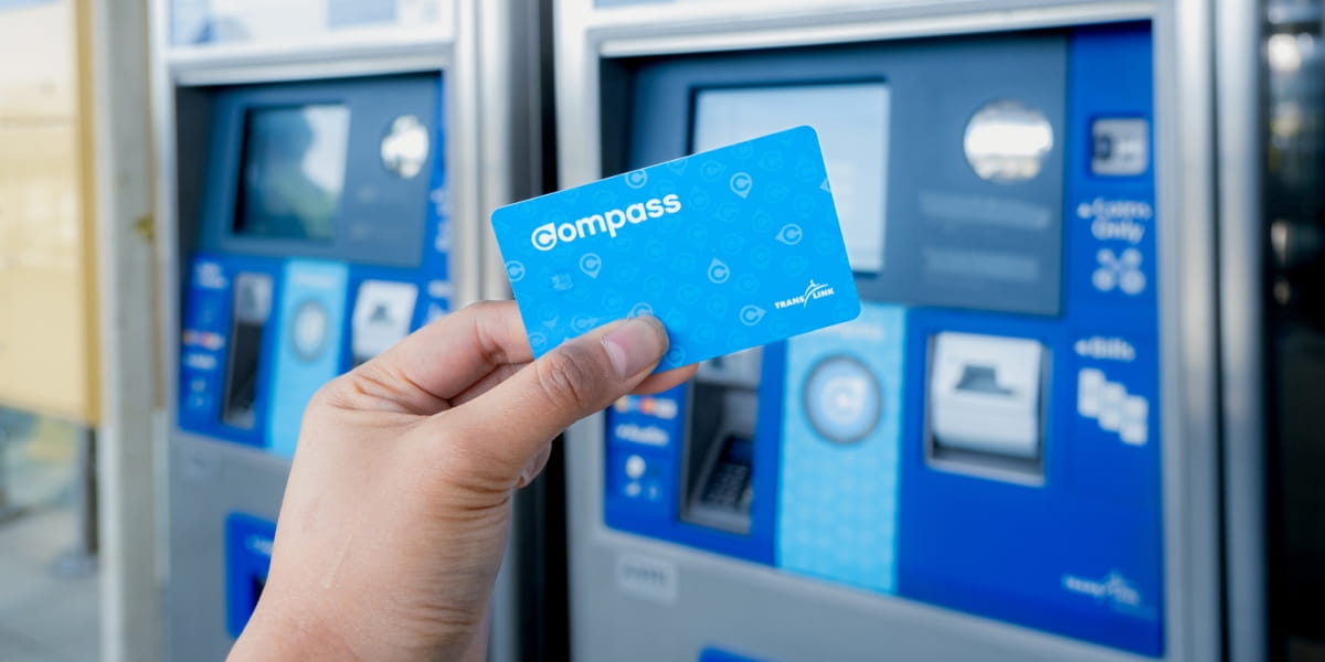 Image of a hand holding a compass card with a Compass Vending Machine in the background