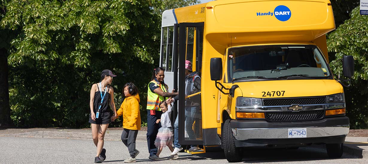 A group of riders disembark from a HandyDART vehicle, with a driver assisting as children and accompanying adults step out.