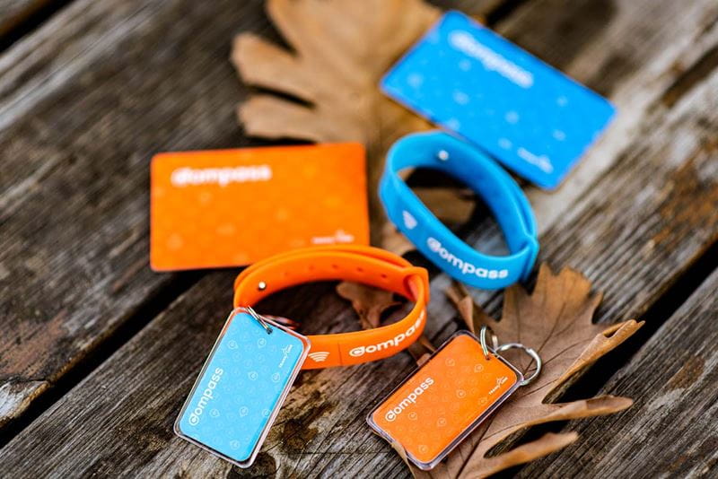 two compass cards, two compass wristbands, and two compass keychains laid out next to withered leaves