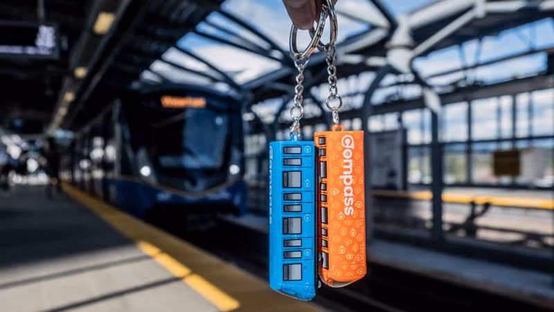 Compass Mini-Train keychains held in front of SkyTrain on station platform