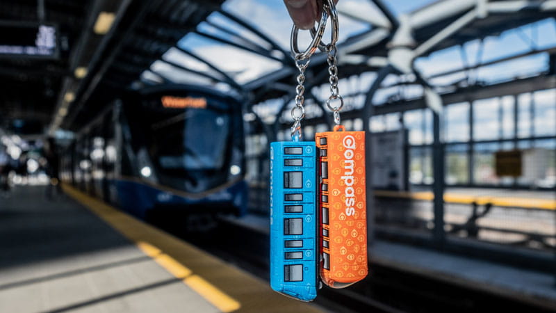 Compass Mini-Train keychains held in front of SkyTrain on station platform
