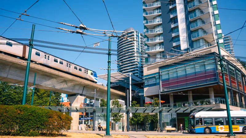 A train arrives at Marine Drive station while passengers wait for a bus at street level
