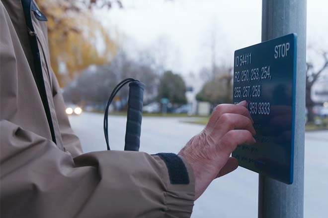 A partially sighted man touching the braille signage attached to a bus stop pole