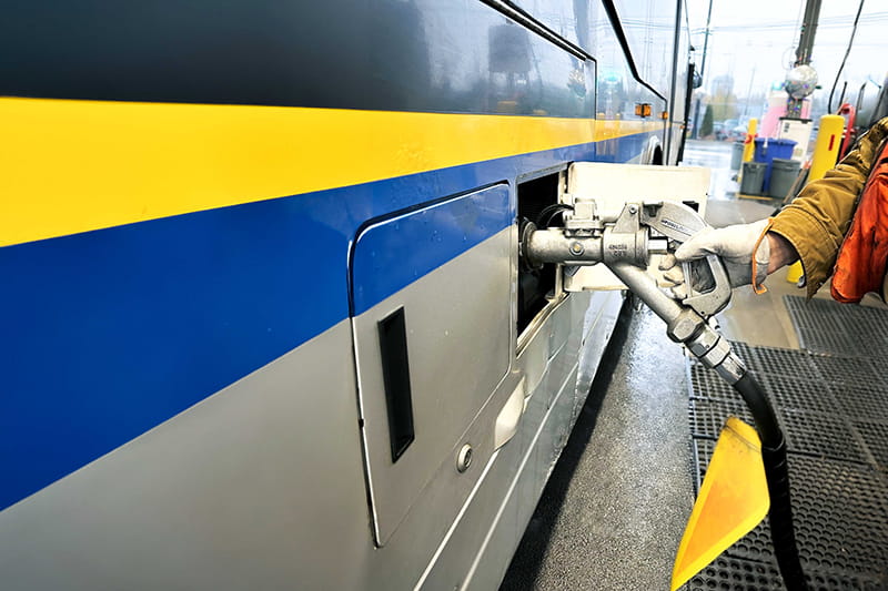 A hand is holding a diesel gas nozzle while it fuels up a bus using renewable diesel