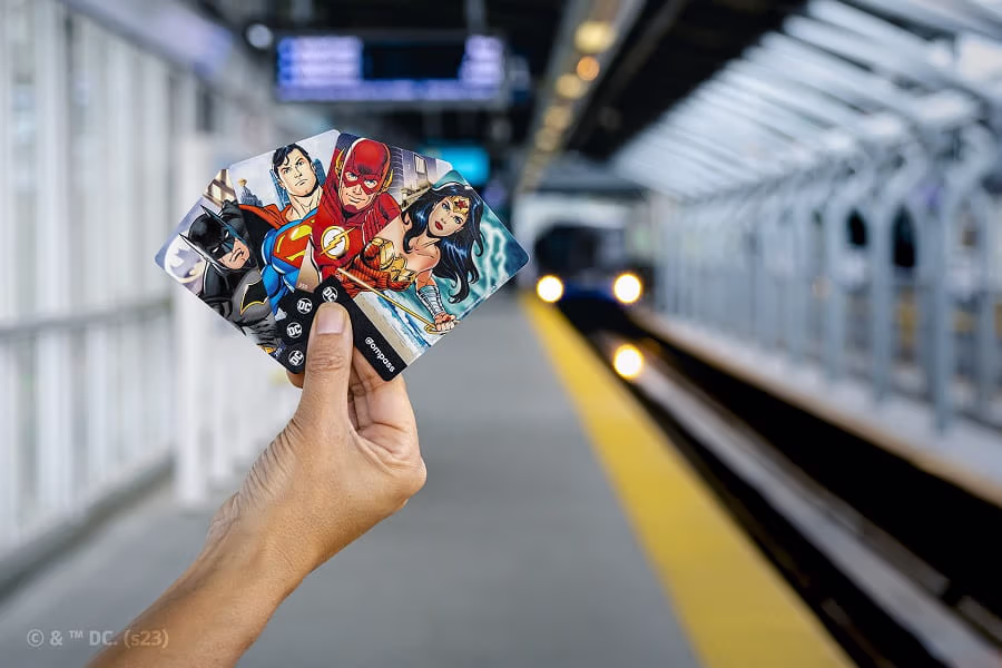 Four DC Super Hero Compass Cards held in front of SkyTrain platform
